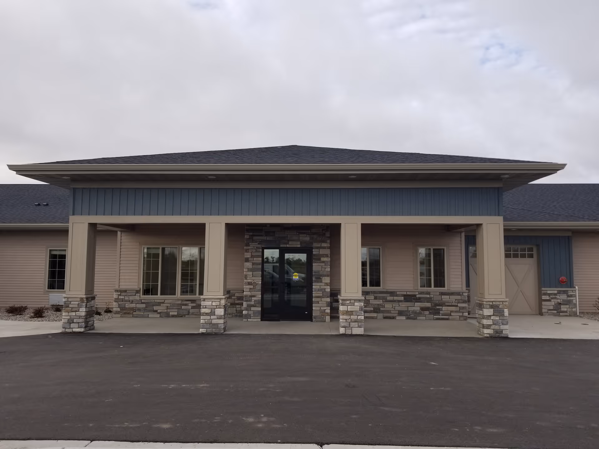 Front entrance of a single-story assisted living building with a covered portico, stone-clad columns, and glass double doors.