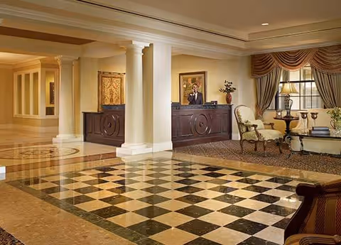 Elegant senior living lobby with a checkered marble floor, reception desk, columns, and a seating area by a window.