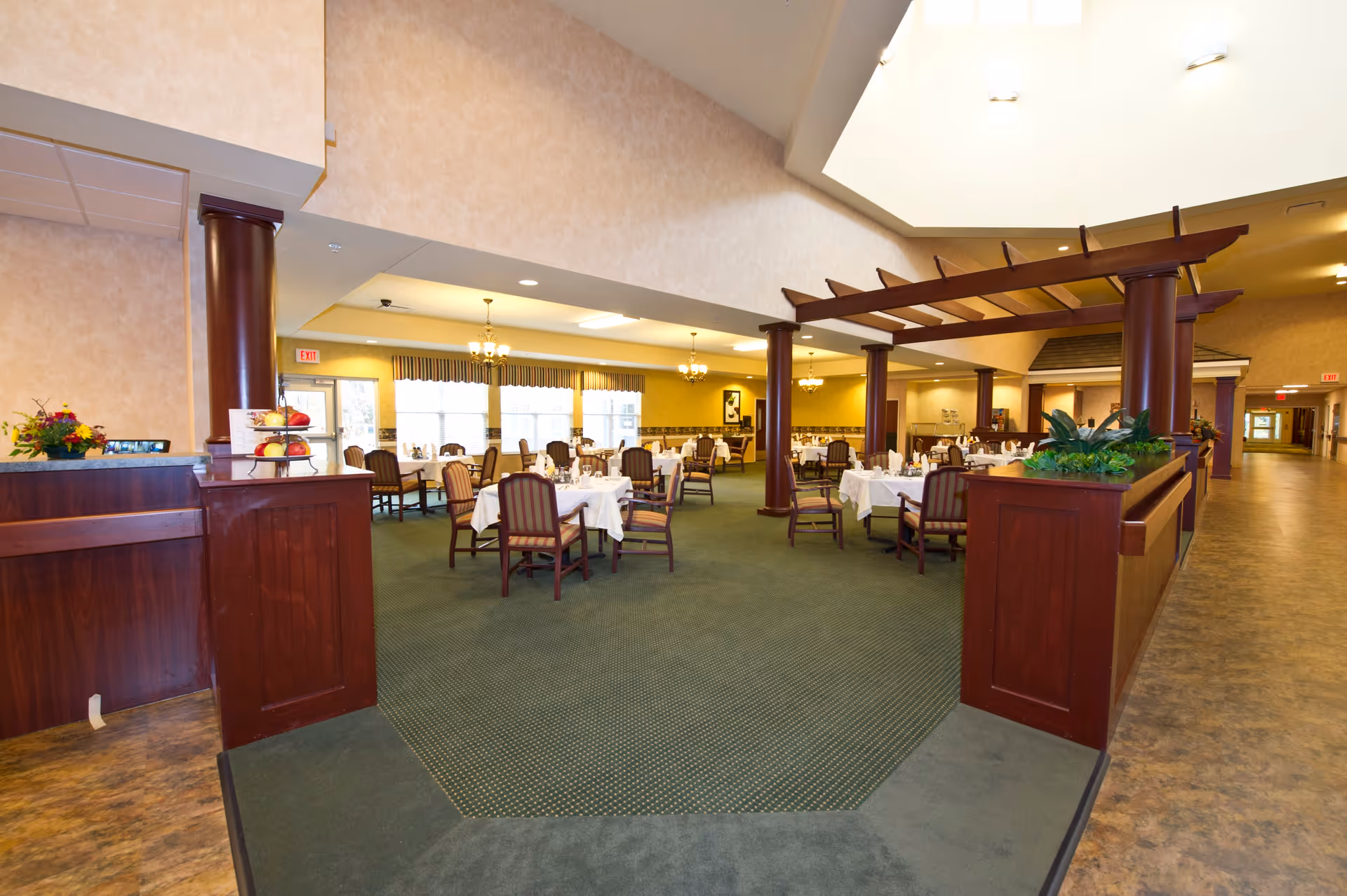 Spacious dining room with tables set with white tablecloths, wooden columns and a pergola-like overhead feature.