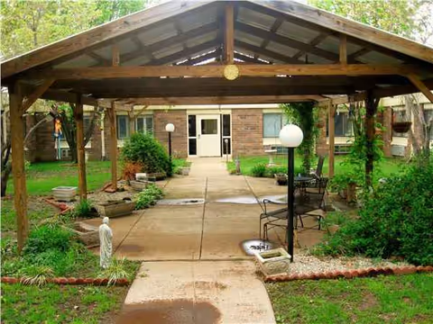Entrance to a senior living facility seen through a wooden gazebo with garden seating.