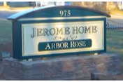 Green-and-white outdoor sign reading "Jerome Home Arbor Rose" with the number 975 on top mounted on a low brick base.