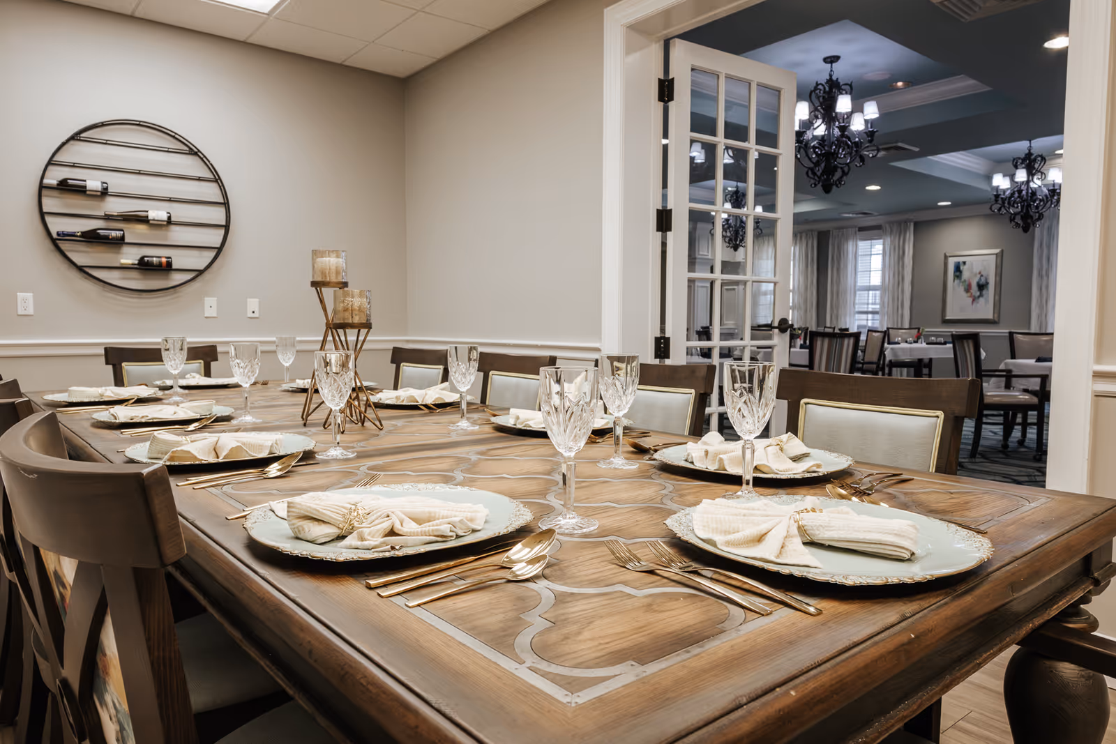 Long wooden dining table set with plates, napkins, and crystal glasses in an elegant indoor dining room.