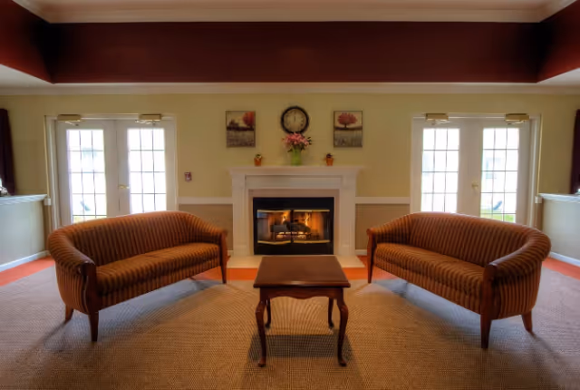 Symmetrical sitting area with two striped sofas facing a lit fireplace and a small wooden table, flanked by French doors.
