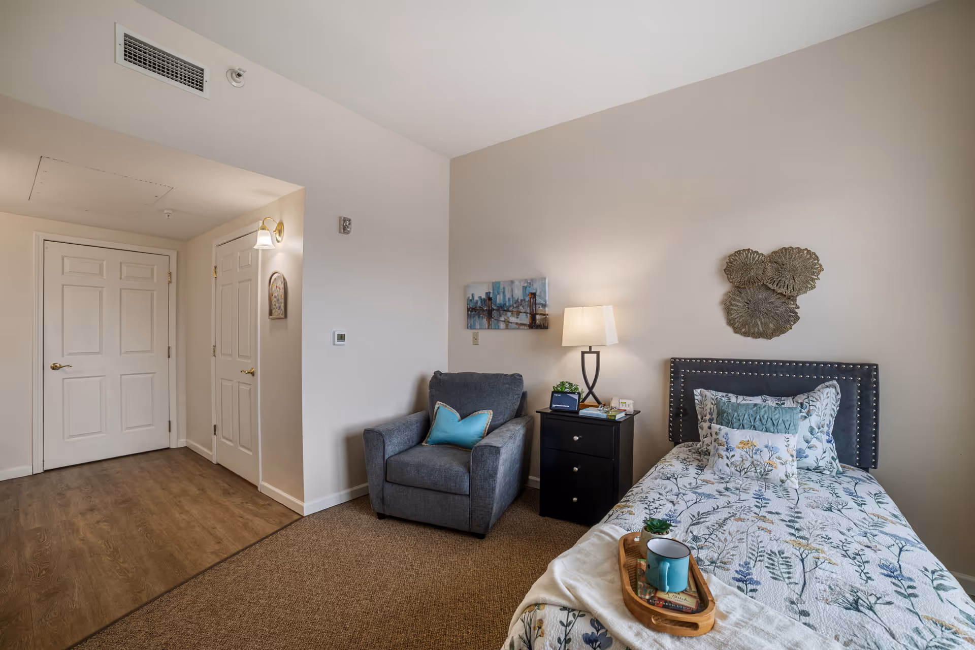 Single-occupancy bedroom with a twin bed, nightstand and lamp, an upholstered chair, and wall decor.