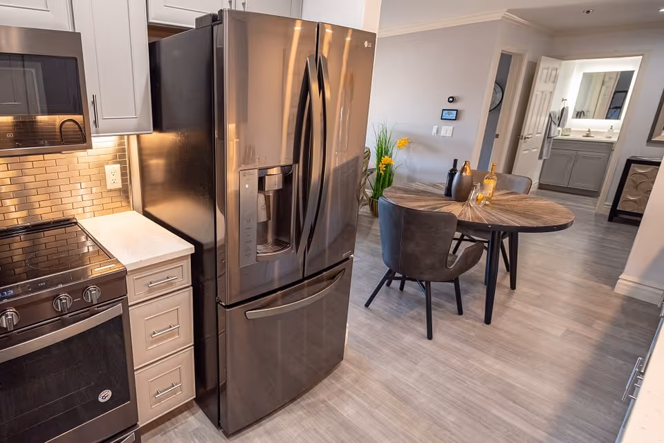 Modern kitchen with a stainless steel refrigerator and stove opening into a small dining area with a round table and chairs.
