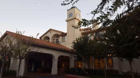 Oakmont of Montecito exterior building with arched entry, tower, and surrounding trees.