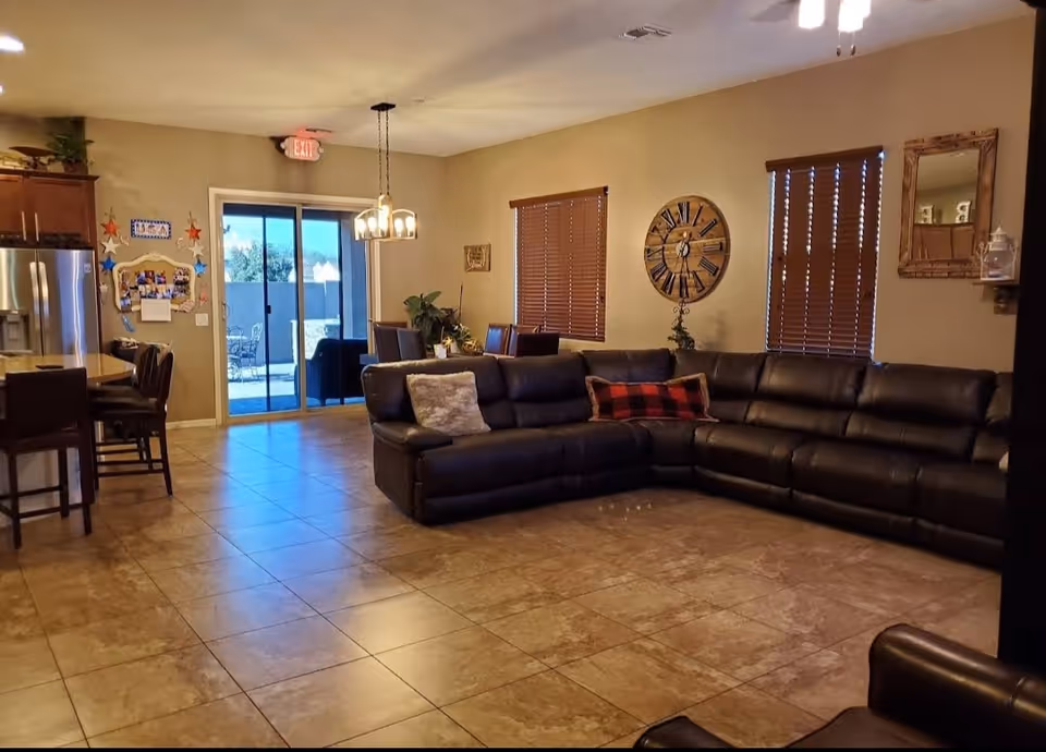 Spacious open living room and kitchen area with a large L-shaped leather sofa, tile floors, dining table, and sliding glass door to a patio.