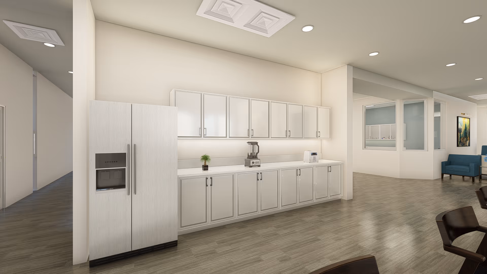 A modern kitchen area with white cabinets and drawers, a side-by-side refrigerator with a water dispenser, a blender, a toaster, and a small potted plant on the countertop. The kitchen opens into a spacious room with wood flooring and a blue armchair visible in the background.