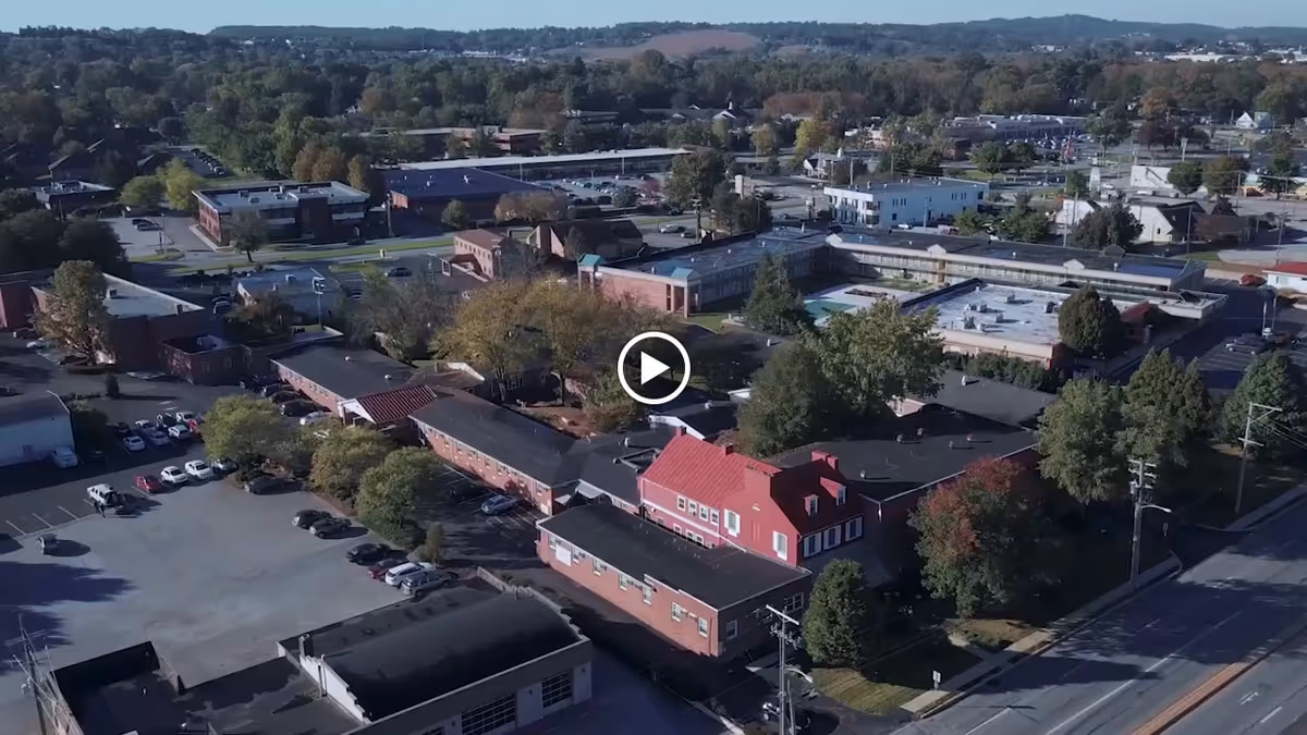 Aerial view of Autumn House East senior living complex with red-roofed buildings, parking lot, and surrounding trees.