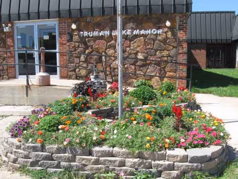 Exterior view of Truman Lake Manor entrance with a colorful circular flower bed in front.