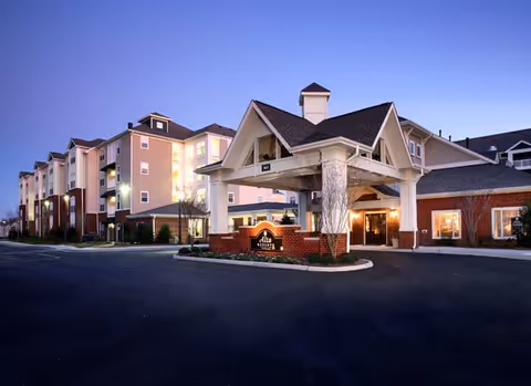 Front entrance and illuminated facade of a multi-story senior living building at dusk.