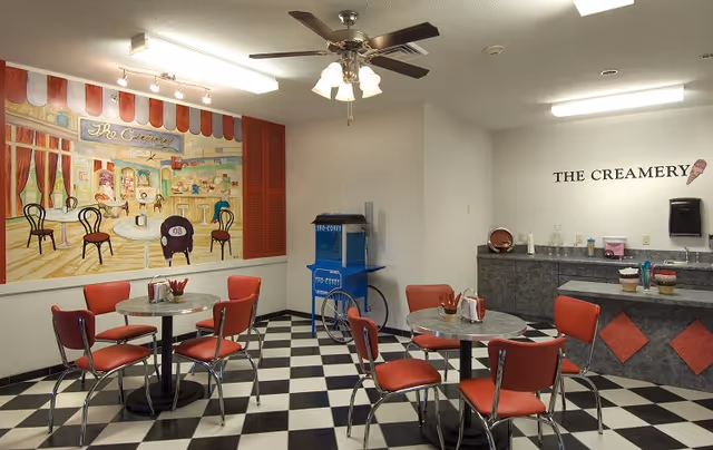 Retro-themed dining area with red vinyl chairs, round tables on a black-and-white checkered floor and a counter labeled "The Creamery".