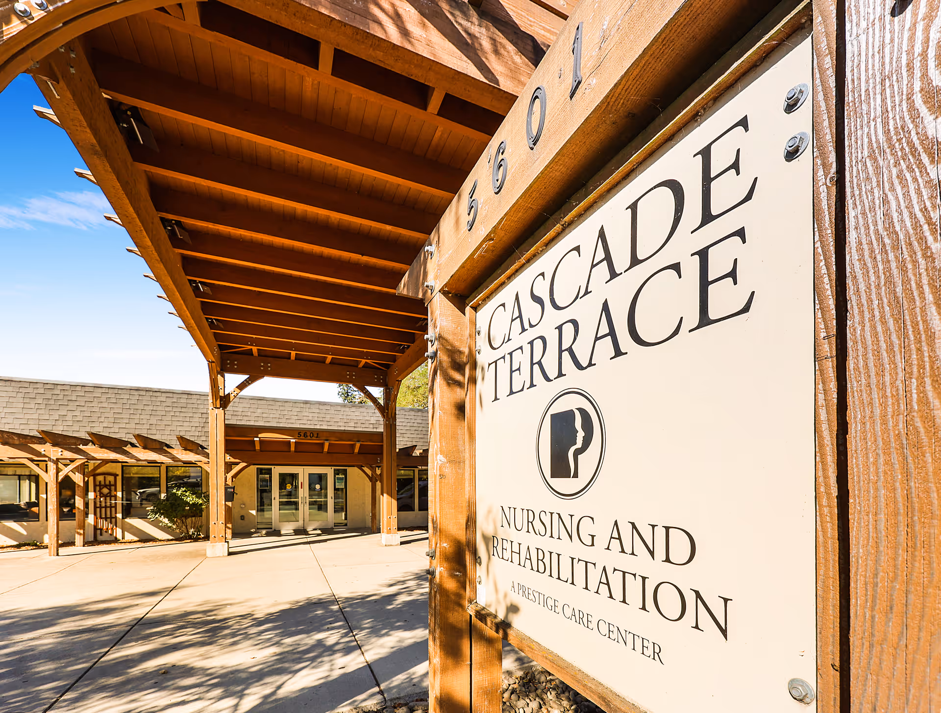 Entrance to Cascade Terrace Nursing and Rehabilitation facility with a wooden pergola structure and a large sign displaying the facility name and logo.