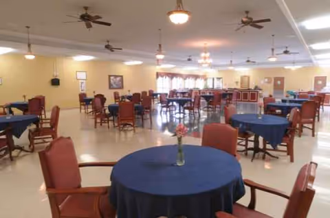Spacious dining hall with round tables, blue tablecloths, and red chairs at Willow Ridge.