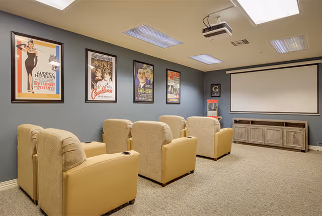 Small screening room with six beige reclining chairs facing a projector screen and classic movie posters on the wall.