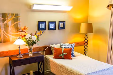 Cozy bedroom in a senior care center with a bed, flowers, and warm lighting.