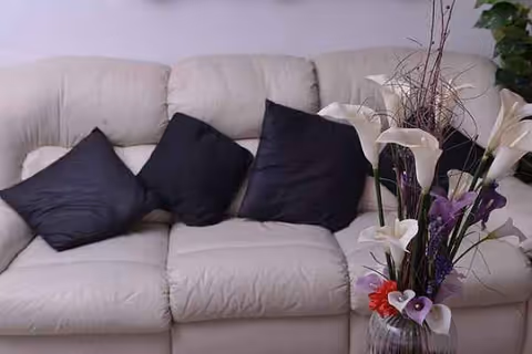 White sectional sofa with black cushions and a tall floral arrangement in a glass vase.