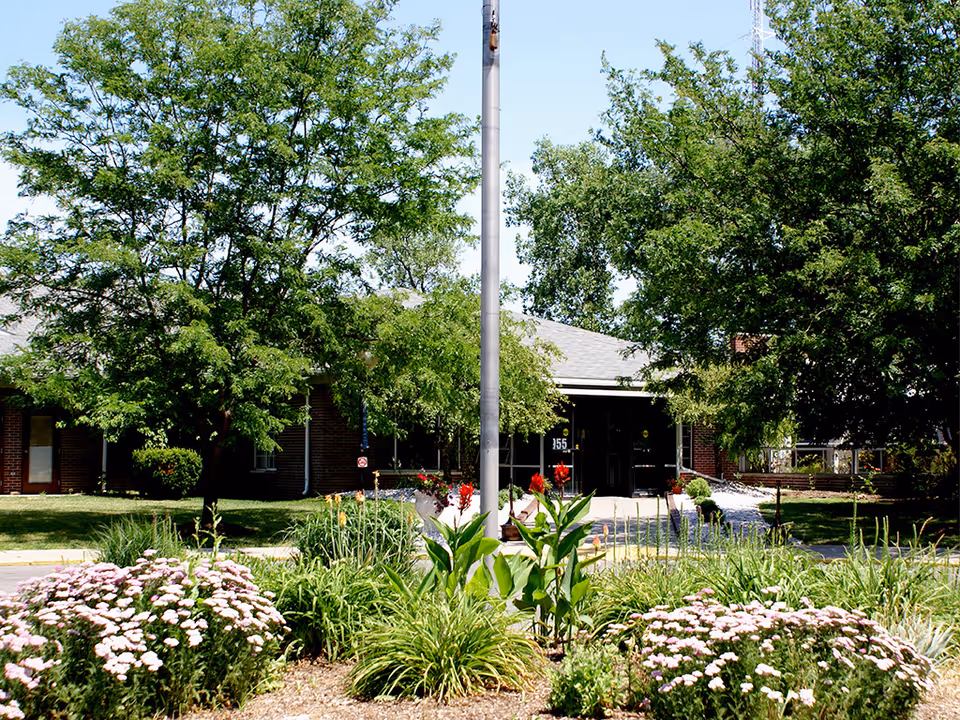 Front exterior of the Advanced Healthcare Center with a landscaped entrance, flagpole, and trees partially obscuring the building.
