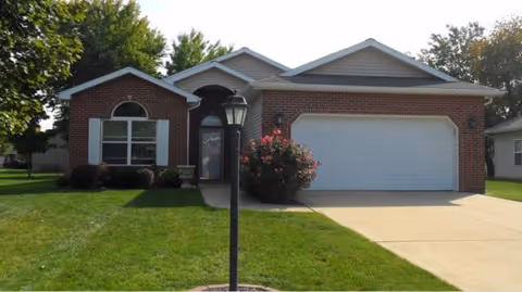 Single-story brick house with attached garage, manicured lawn, and a street lamp.