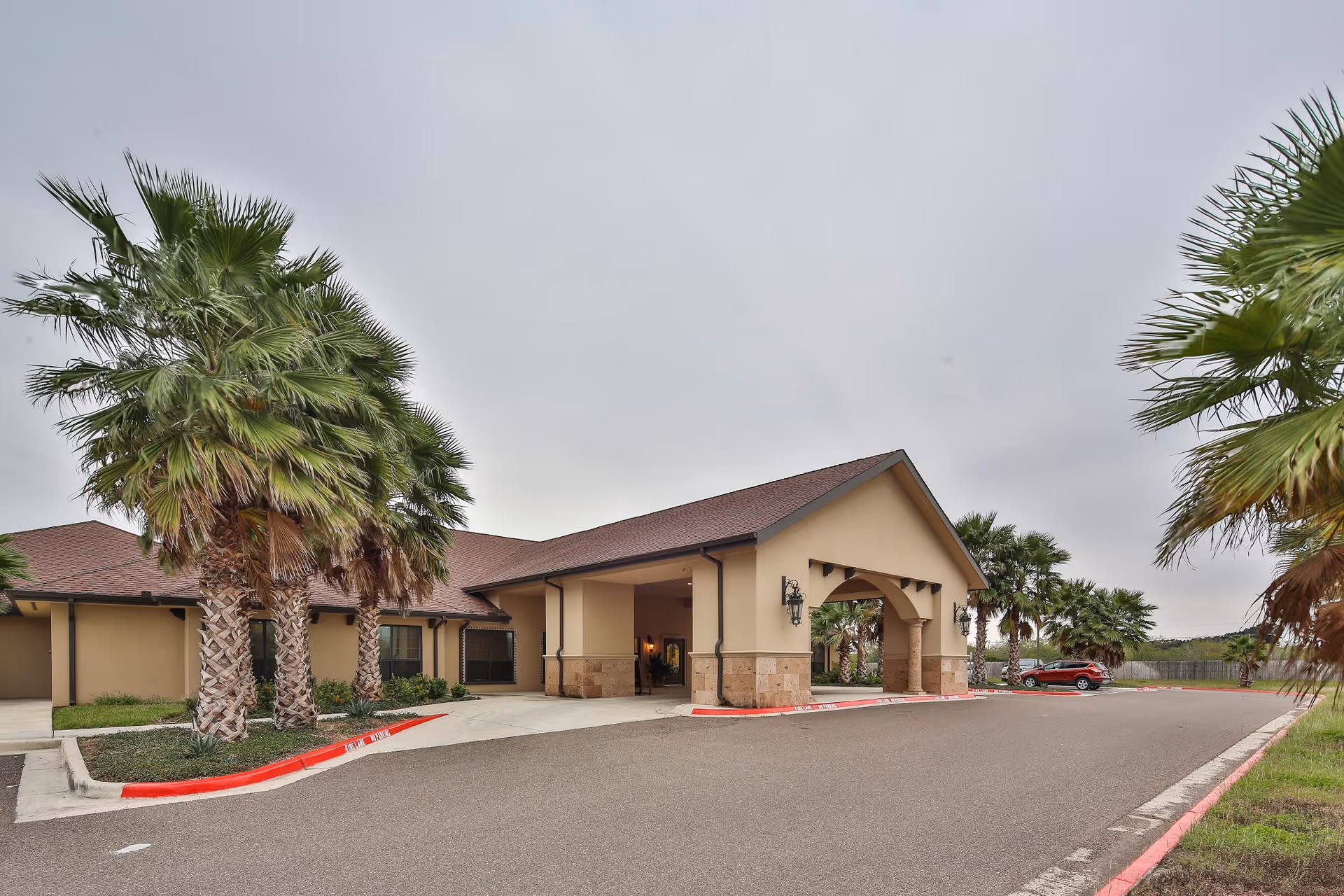 Covered front entrance of a single-story building with palm trees and a driveway.