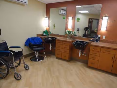 Hair salon area inside a senior living facility with mirrors, sinks, and a wheelchair.