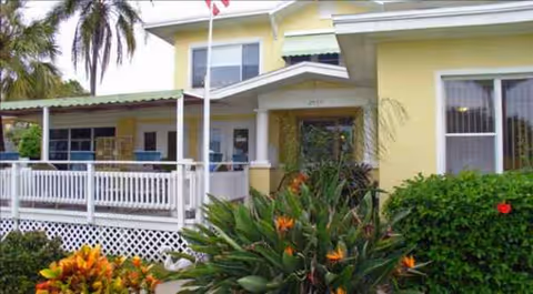 Exterior view of Edgewater Retirement Manor: yellow building with front porch and tropical plants.