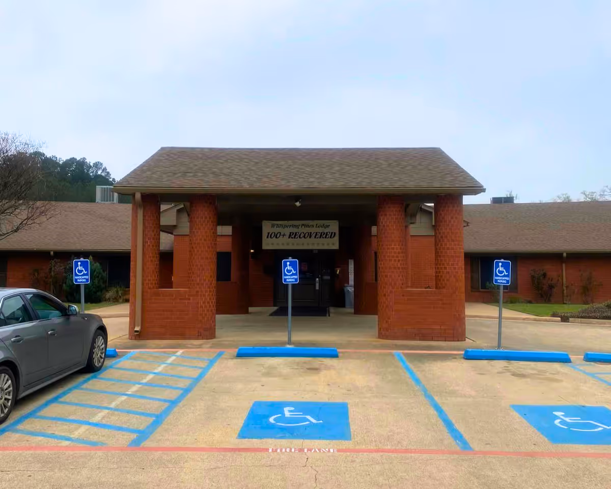 Entrance of a brick senior living facility with a covered portico and marked handicap parking spaces and signs in front.