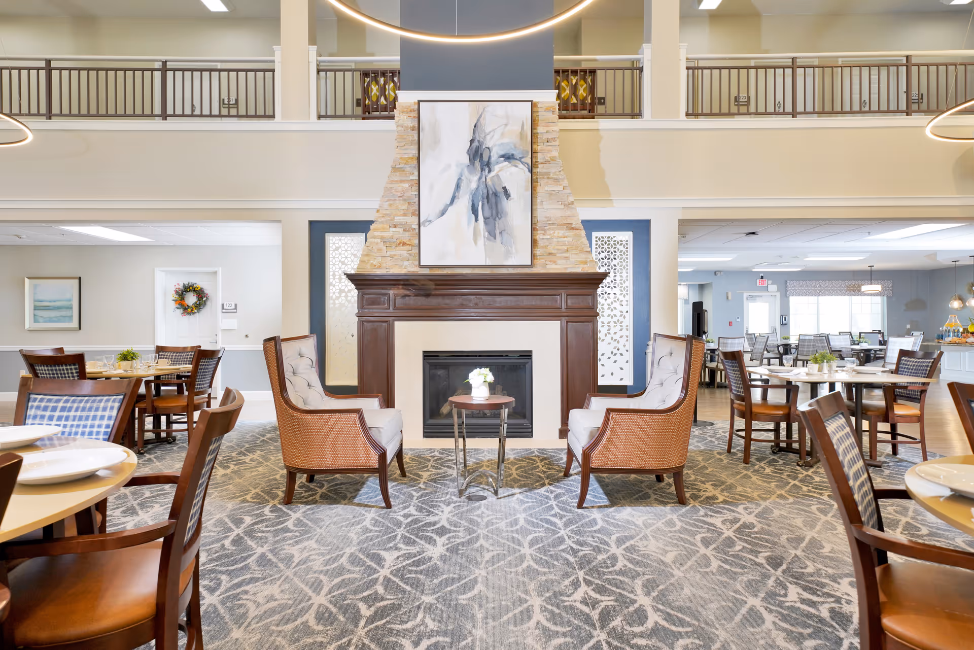 Bright communal dining and lounge area with a central fireplace, chairs, and dining tables.