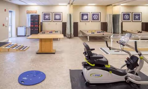 Therapy room with stationary bike, balance boards, and therapy tables.