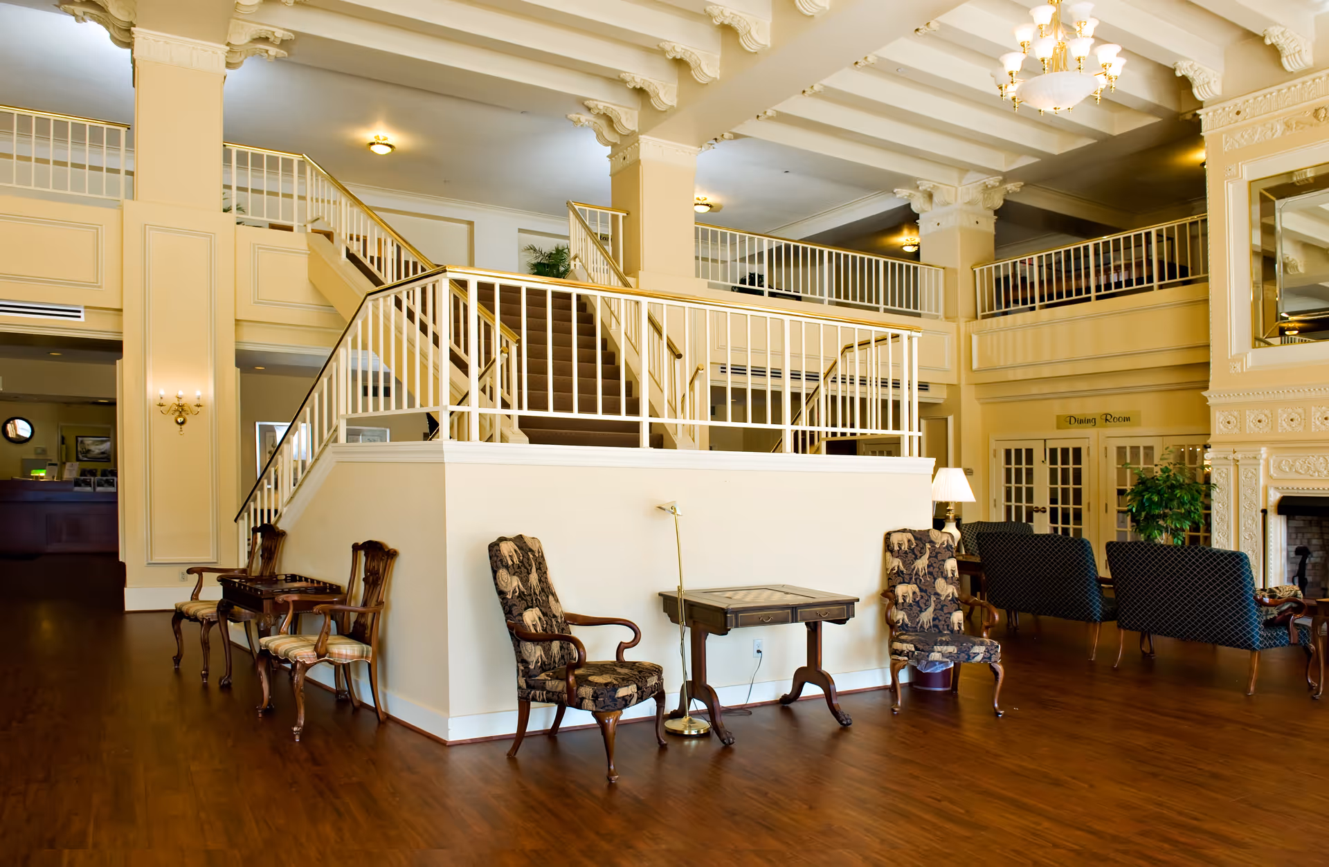 Spacious, elegant senior living lobby with a central staircase, seating areas, and ornate columns and chandeliers.