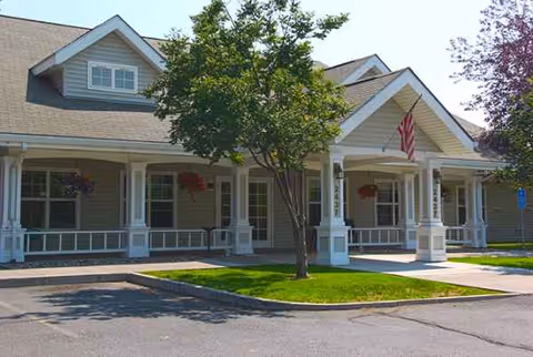 Exterior of a senior living facility with a covered porch, white columns, and a tree.