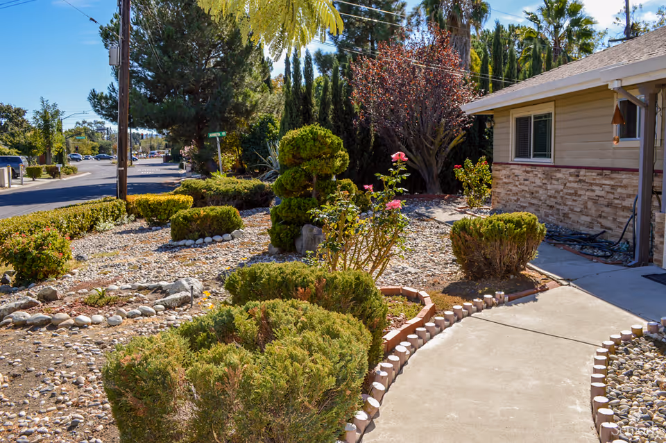 Front yard and walkway of a single-story house with a landscaped rock garden, shrubs, and a path leading to the entrance.