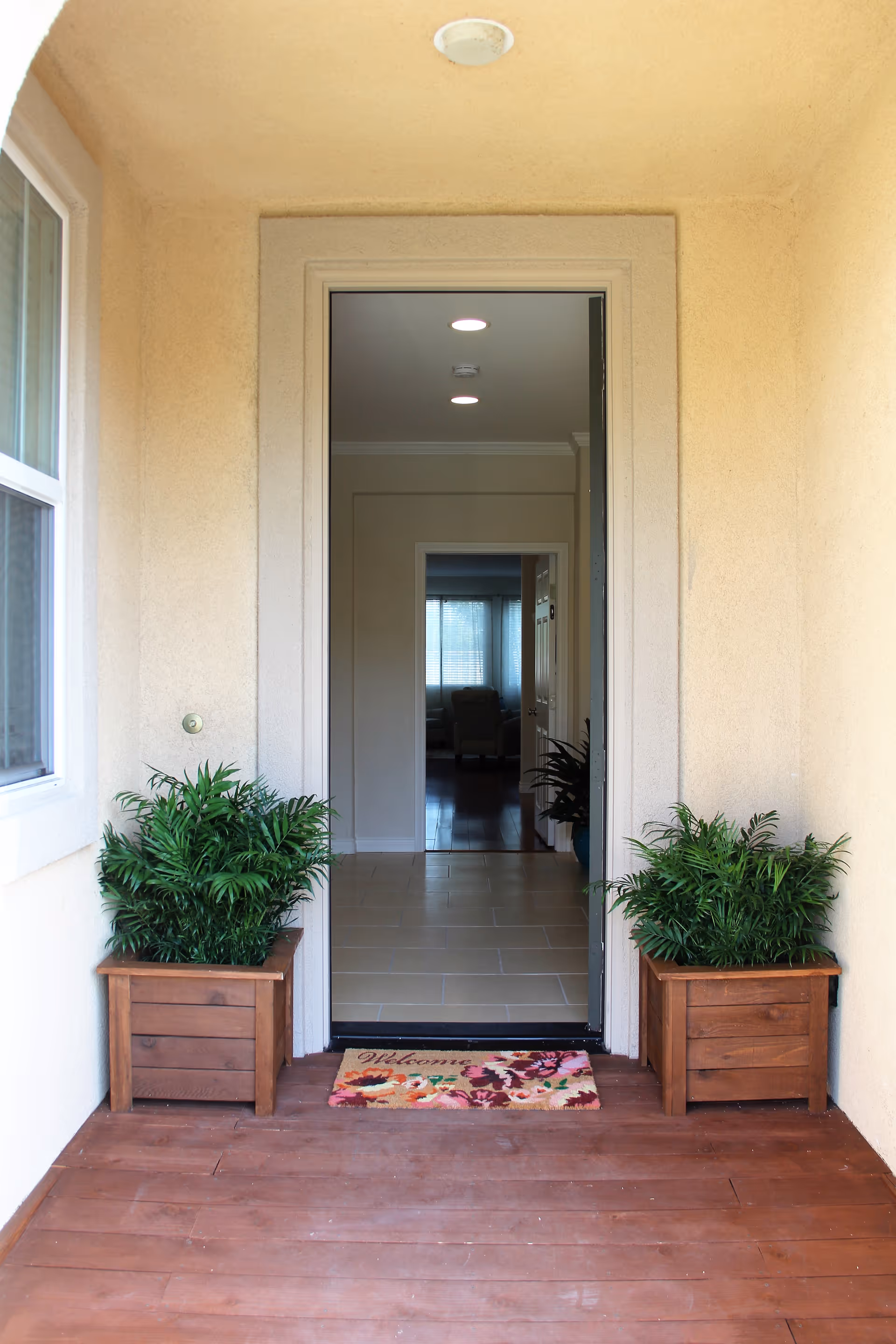 Front entryway with an open door flanked by two potted plants and a welcome mat leading into the interior.