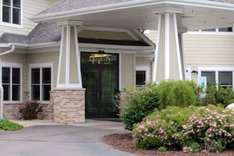 Front entrance of a senior living facility with a covered porte-cochere and landscaped bushes.