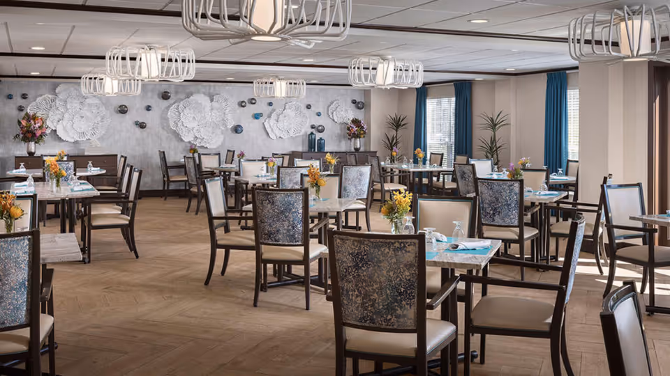 Bright, modern dining room with multiple tables and chairs, pendant lights, floral centerpieces, and decorative wall art.