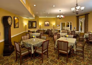 A warmly lit dining room with several tables and chairs in a senior living facility.