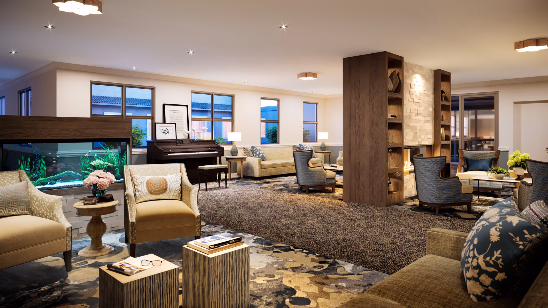 A spacious and well-lit living room area in a senior living facility featuring multiple seating arrangements with armchairs and sofas, a large aquarium, a piano, decorative pillows, side tables with lamps, a fireplace with built-in shelves, and large windows letting in natural light.