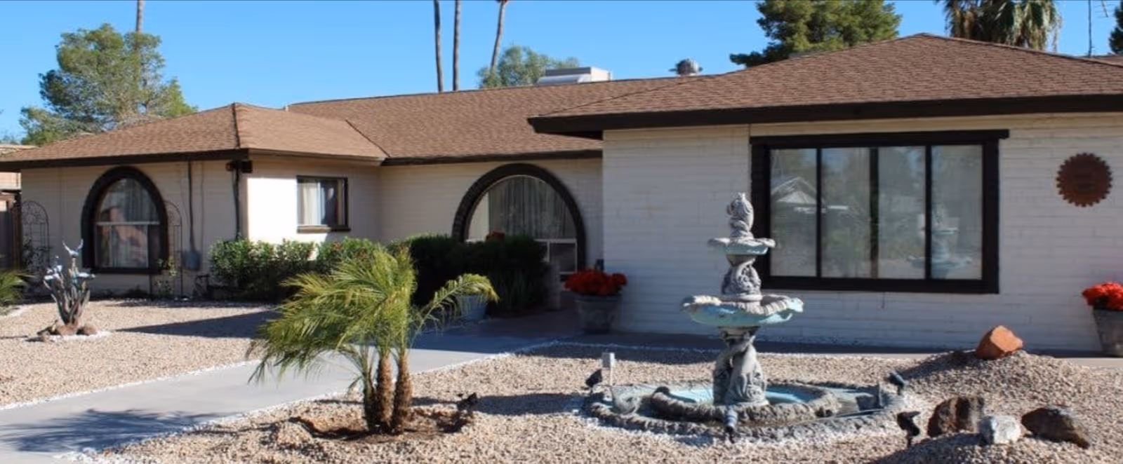 Single-story assisted living building front with a tiered fountain and desert rock landscaping in the front yard.