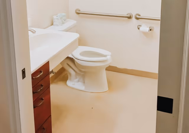 Accessible bathroom with a toilet, sink vanity, grab bars, and a toilet paper holder.