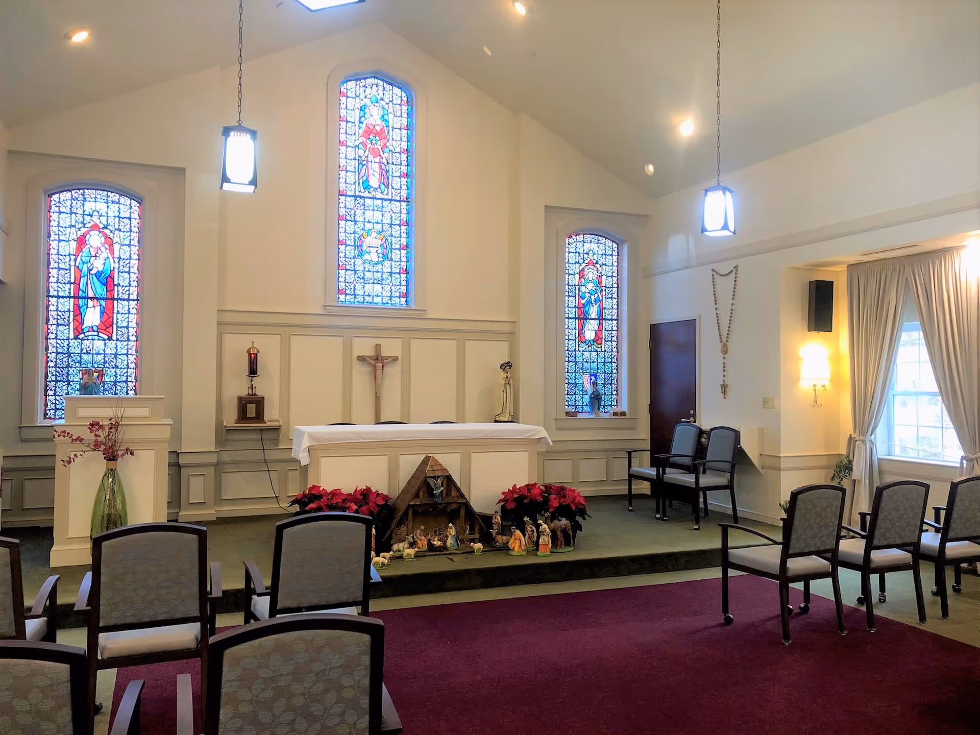 Interior of a chapel featuring stained glass windows, an altar with a white cloth, and seating arranged in front.