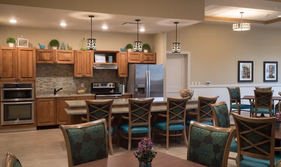 Communal kitchen and dining area with a long island, wooden cabinets, stainless steel appliances, and multiple dining tables and chairs.