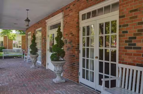 Brick-walled porch with French doors, white benches, and decorative topiary planters.