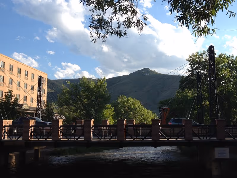 Exterior view of a brick bridge with cars, trees, and mountains in the background.