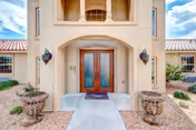 Stucco building entrance with double wooden doors, decorative urn planters, wall sconces, and a covered entryway.