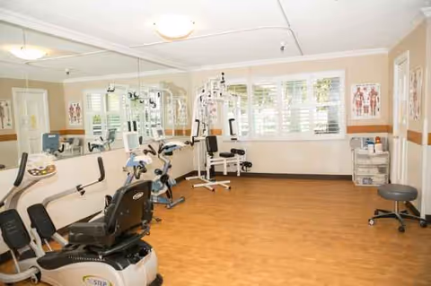An empty senior living fitness room with stationary bikes, a multi-gym, and mats.