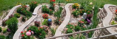 Colorful flower beds bordered by brick edging along a garden path with railing.