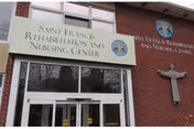 Front entrance of Saint Francis Rehabilitation and Nursing Center showing signage, glass doors, and a wall-mounted statue on a brick facade.
