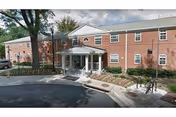 Two-story red brick assisted living residence front entrance with a covered portico, circular driveway, and landscaped beds.