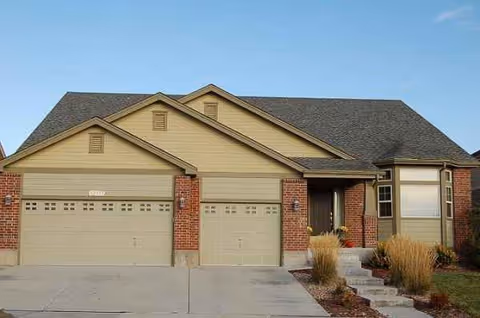 Front view of a beige suburban home with three-car garage and landscaped yard.