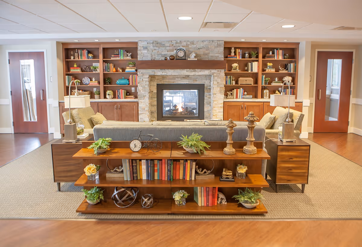 Communal living room with a central stone fireplace, built-in bookshelves, a sofa, and decorative shelving and plants.